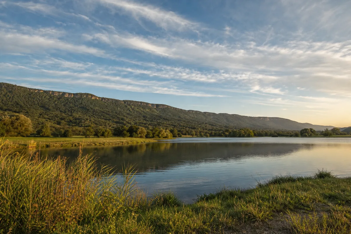 Lac de plaine bordé de prairies avec une longue crête boisée en arrière-plan en fin d&rsquo;après-midi